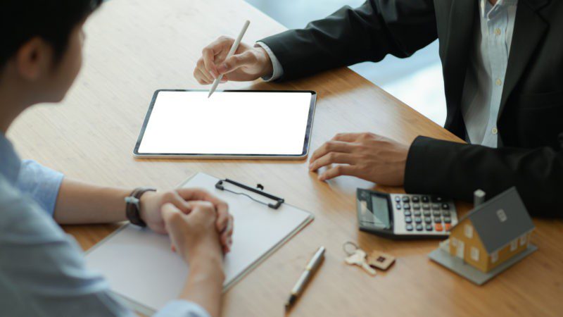 two people with tablet and clipboard talking on wood desk